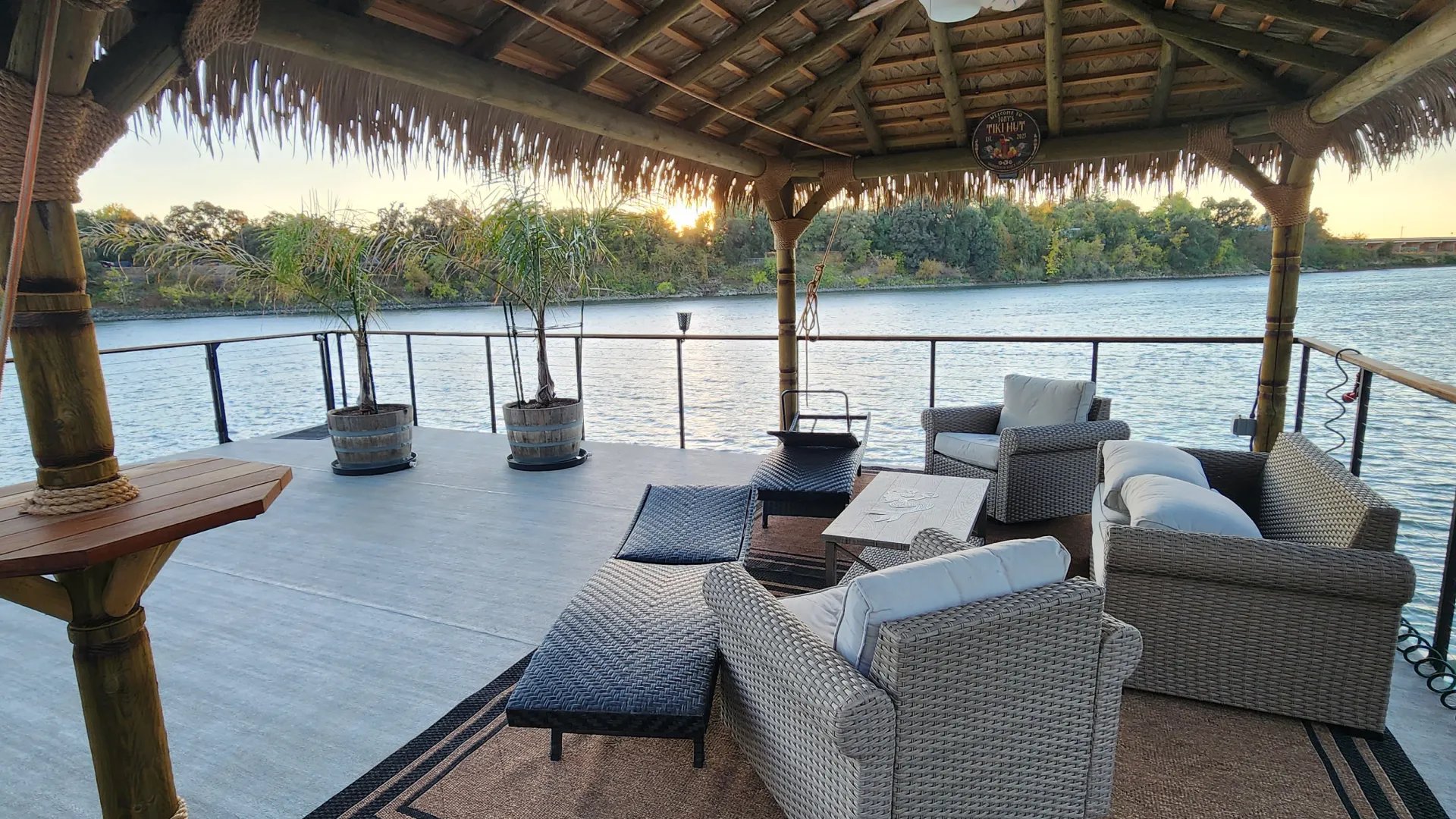 Lakeside deck under a thatched palapa with lounge seating at sunset